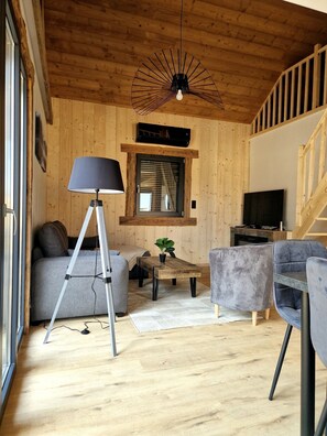 A cozy living room with a wooden ceiling, a sofa, a coffee table, a lamp, and a television. - "LSN6" Chalet: Cozy & High-End Comfort with Sauna, Spa, Air Conditioning, Foosball, and Pool (Anould)