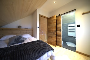 A bedroom with a wooden ceiling, a bed with white bedding, a black blanket, and a wooden wardrobe with a sliding door. - Cozy, high-end chalet with sauna, spa, air conditioning, foosball, and a pool (Anould)