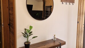 Una consola de madera con una planta en maceta y un adorno pequeño, un espejo redondo en la pared y un banco de madera con ganchos.