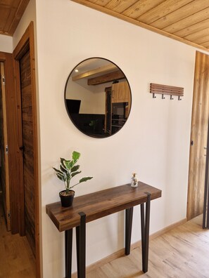 A wooden console table with a potted plant and a small decorative item, a round mirror on the wall, and a wooden bench with hooks. - "LSN6" Chalet: Cozy & High-End Comfort with Sauna, Spa, Air Conditioning, Foosball, and Pool (Anould)