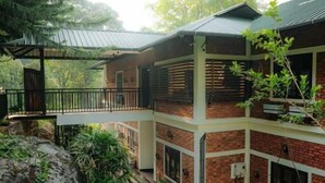 A two-story building with a brick facade, a covered patio, and a small garden area. - Aroma Hills Resort (Udumbanchola)