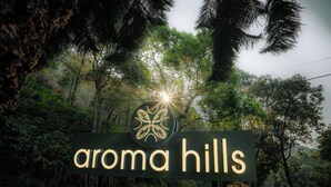 A sign for 'Aroma Hills' with a logo, surrounded by lush greenery. - Aroma Hills Resort (Udumbanchola)