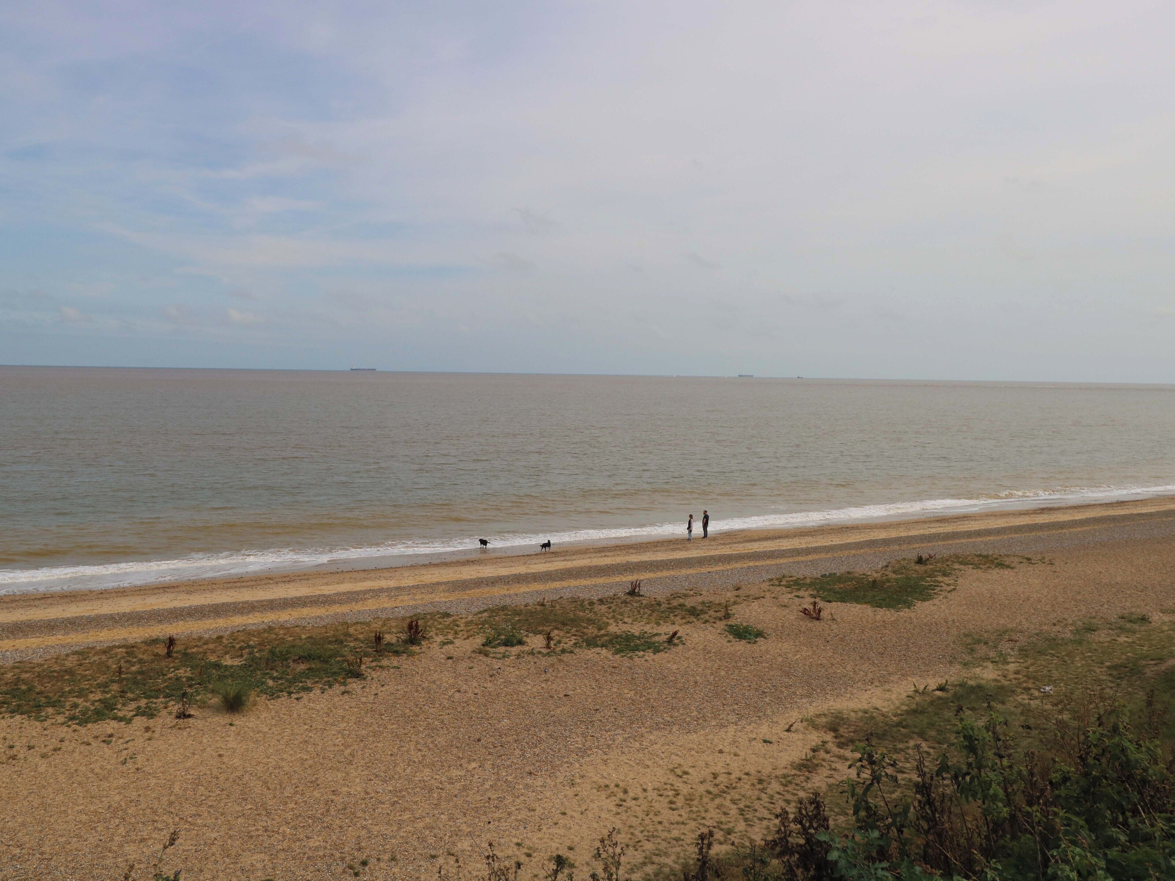 A beach with a wide sandy shore, a few people, and a calm sea.