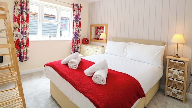 Een hotelkamer met een bed, nachtkastje, lamp, spiegel, raam met gordijnen en een houten trap.