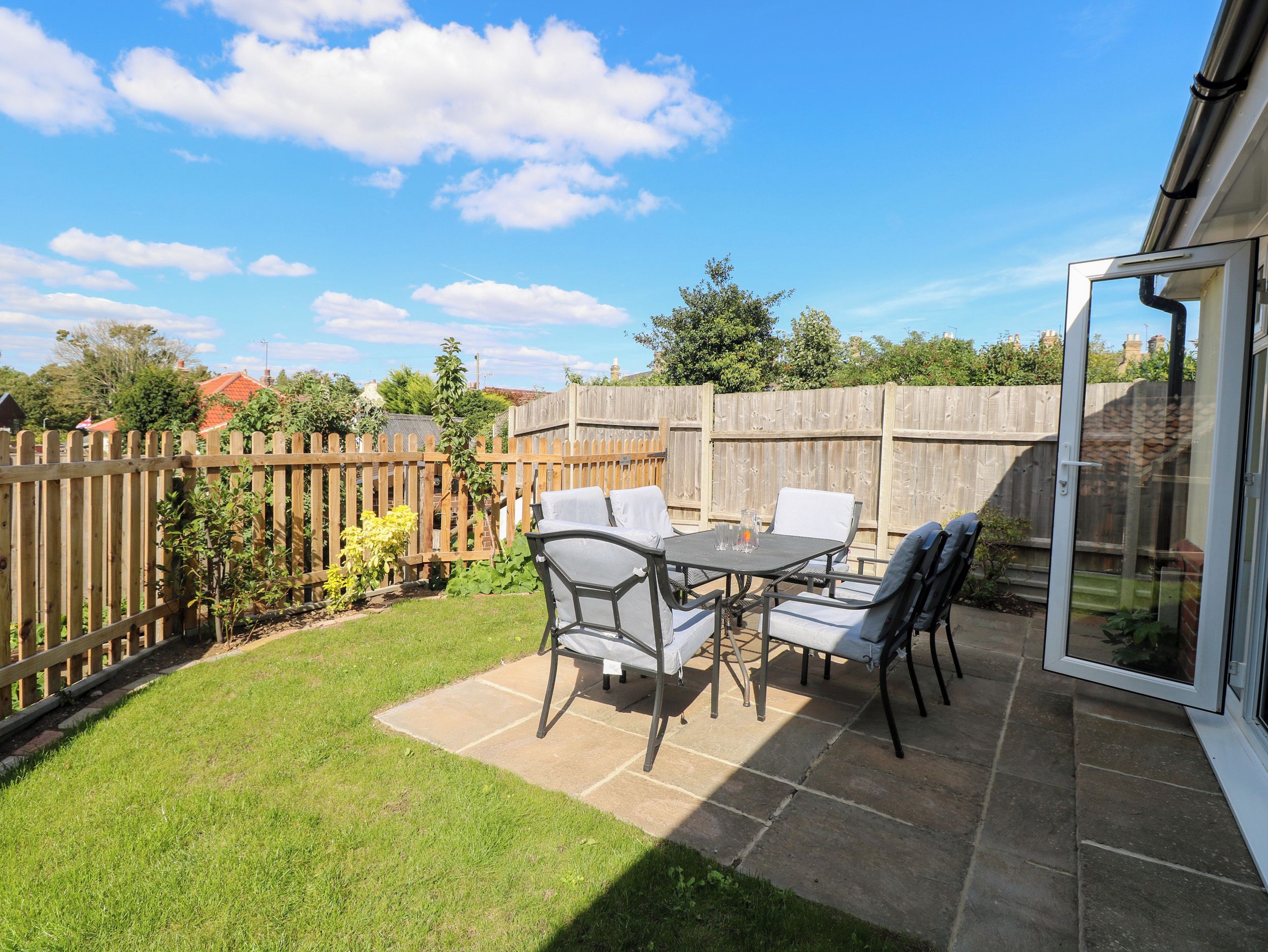 An outdoor patio with a table and chairs, a wooden fence, and a grassy area.