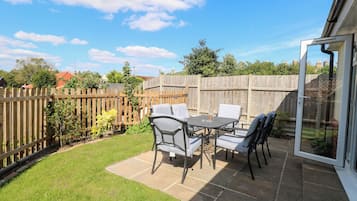 An outdoor patio with a table and chairs, a wooden fence, and a grassy area.