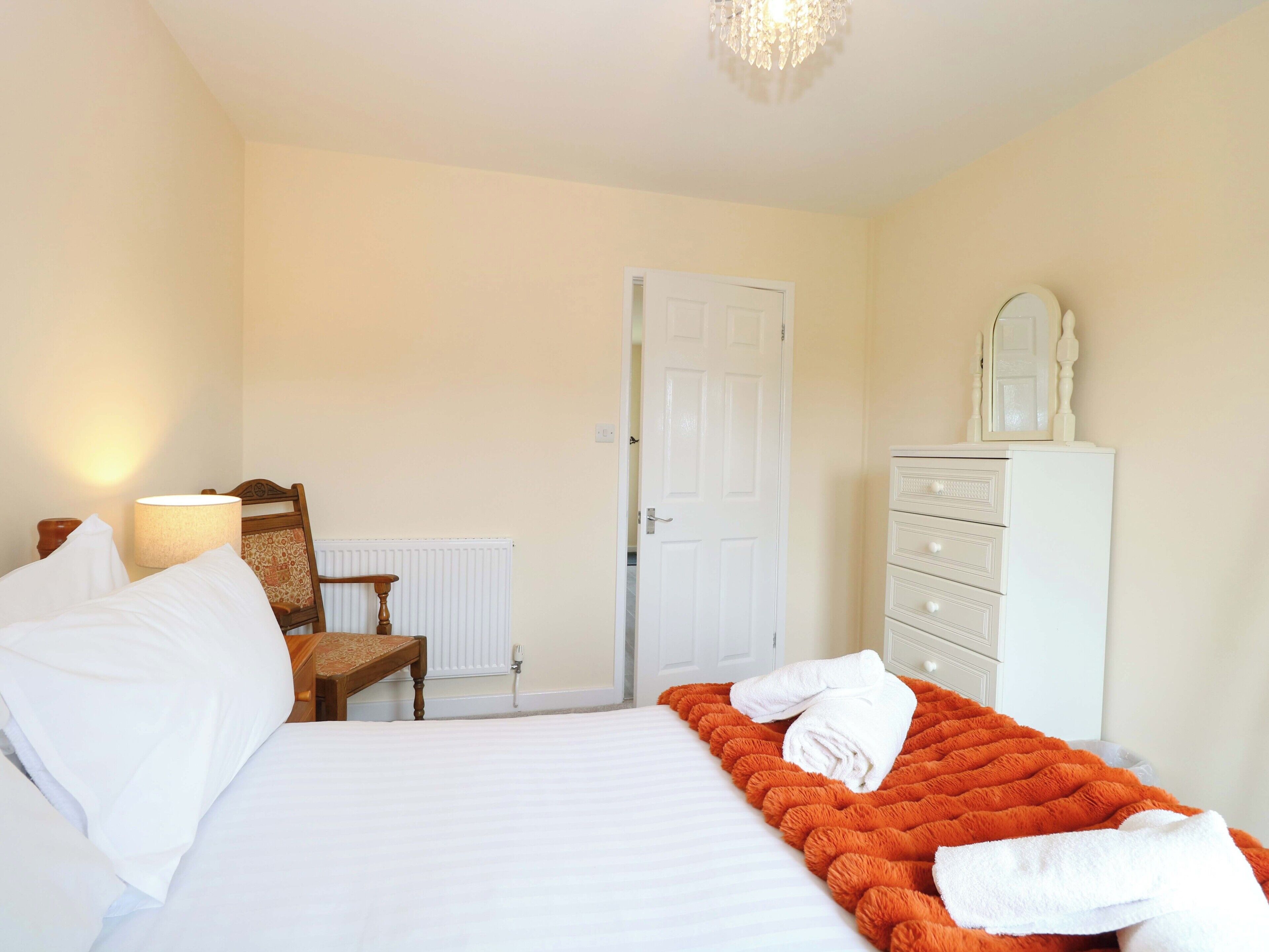 A bedroom with a bed, a chair, a dresser, a mirror, and a radiator.