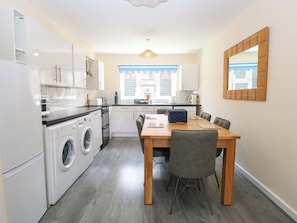 A compact kitchen with a washing machine, a dining table with chairs, and a large mirror on the wall.