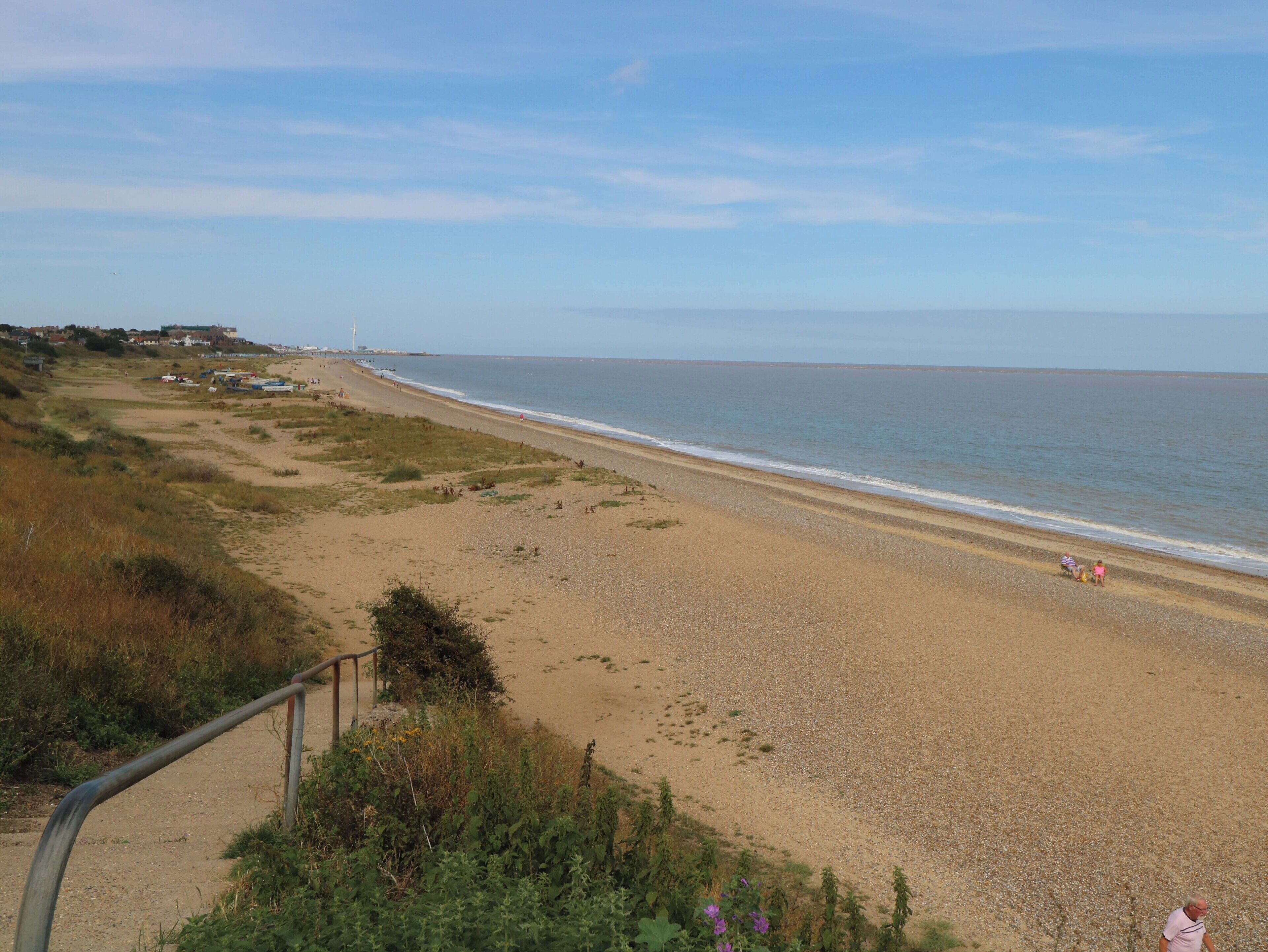A beach with a path leading to the shore, a distant windmill, and a clear sky.