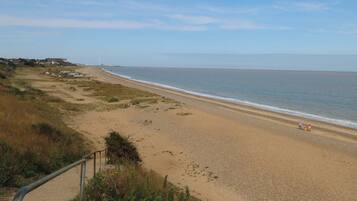 A beach with a path leading to the shore, a distant windmill, and a clear sky.