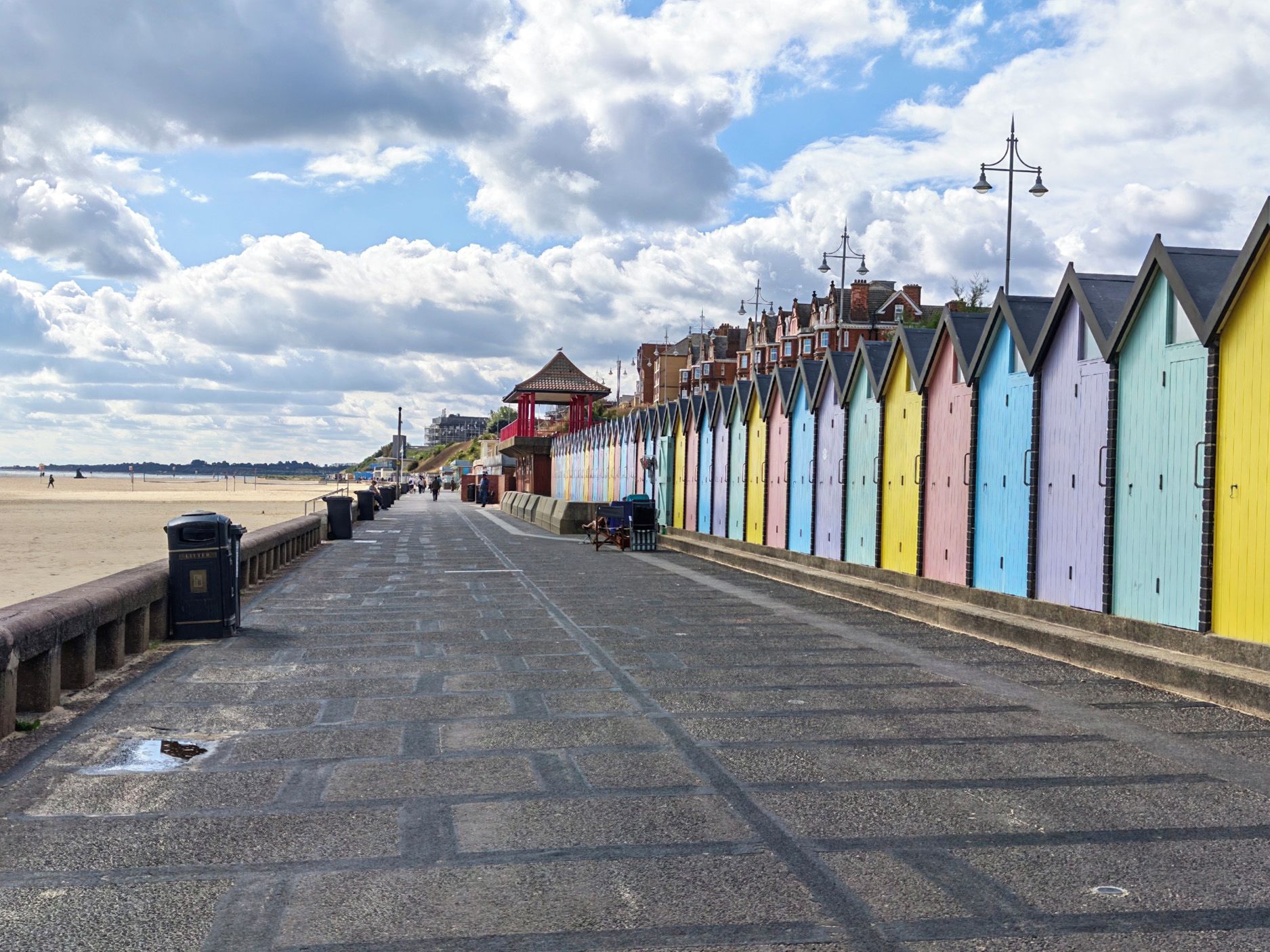 A promenade with colorful beach huts, a gazebo, and a beach in the background.