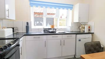 Una cocina moderna con gabinetes blancos, una estufa negra, un lavavajillas y una ventana con vistas al exterior.