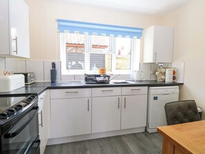 A modern kitchen with white cabinets, a black stove, a dishwasher, and a window with a view of the outside. - The Mill House Gardens (Lowestoft)