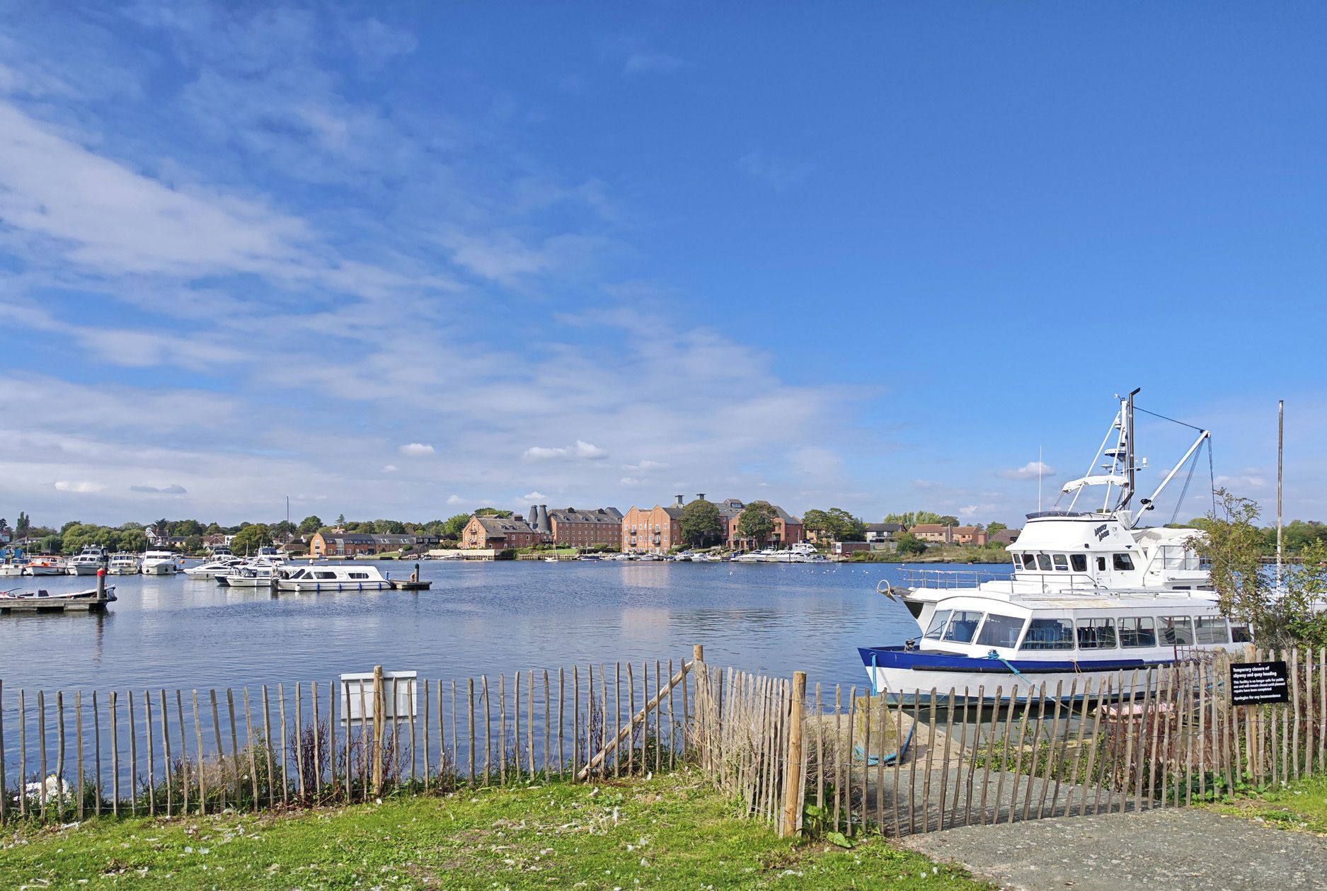 A marina with boats docked, a wooden fence, and buildings in the background.