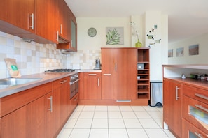 Eine Küche mit Holzausstattung, gefliestem Rückspritzschutz, einer Uhr und einer Pflanze.