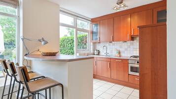Een keuken met houten kastjes, een aanrecht, een spoelbak, een fornuis en een raam met uitzicht op groen.