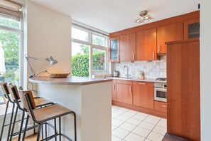 A kitchen with wooden cabinets, a countertop, a sink, a stove, and a window with a view of greenery. - Family House Fahrenheit - dunes, garden and room for six (Zandvoort)
