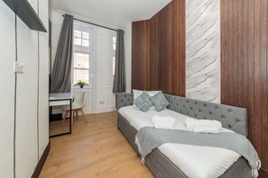 Ein Schlafzimmer mit Bett, Schreibtisch und Stuhl, Holzboden und Blick auf Gebäude.