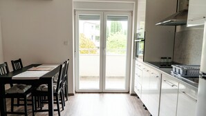 Eine moderne Küche mit weißen Schränken, ein Essbereich mit Tisch und Stühlen sowie eine Glastür, die auf einen Balkon führt.