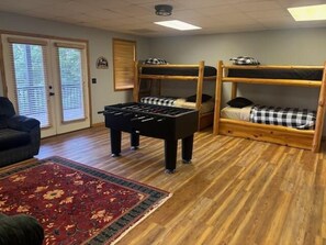 Ein Zimmer mit Etagenbetten, einem Kicker, einem roten Teppich mit Muster und einer Tür mit Jalousien.