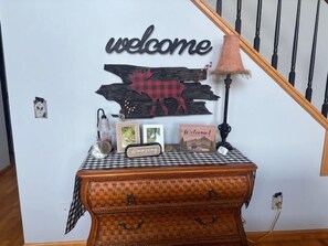 Eine Treppe mit einem 'welcome'-Schild, eine rustikale Holzverkleidung und ein Tisch mit kariertem Tischlauf.