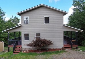 Ein zweigeschossiges Haus mit einer Veranda, einem kleinen Baum und einem Steinfundament.
