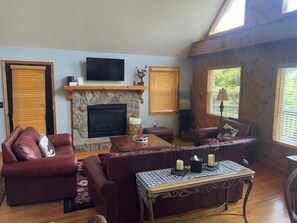 Ein Wohnzimmer mit Kamin aus Stein, Ledersofas, einem Couchtisch und einem Fernseher, der über dem Kamin angebracht ist.