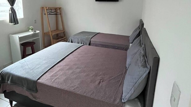 Een slaapkamer met een bed, bureau, stoel, televisie en een raam met gordijnen.