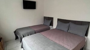 Een kamer met twee bedden, een wandtelevisie en betegelde vloer.