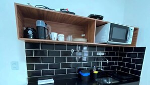Een keuken met een zwart aanrecht, houten kastjes, een magnetron en een koffiezetapparaat.