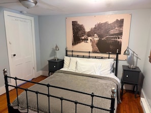 Quarto com cama, mesas de cabeceira, uma porta e um quadro na parede.