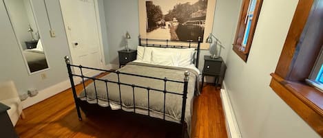 A bedroom with a bed, bedside tables, a mirror, a wall-mounted picture, and a window.