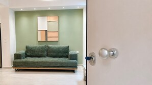 A modern interior with a green sofa, a minimalist wall art piece, and a door with a silver handle. - Galleria Romvis – VΙ by ΜΡS (Athina)