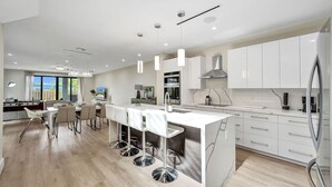Una cocina moderna con armarios blancos, una isla central con taburetes y vistas al exterior.
