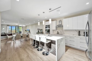Een moderne keuken met witte kasten, een centraal eiland met barstoelen en uitzicht op de omgeving.