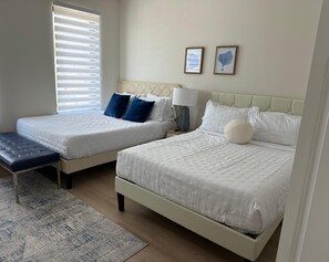 Un dormitorio con dos camas, un banco, una alfombra y dos cuadros en la pared.