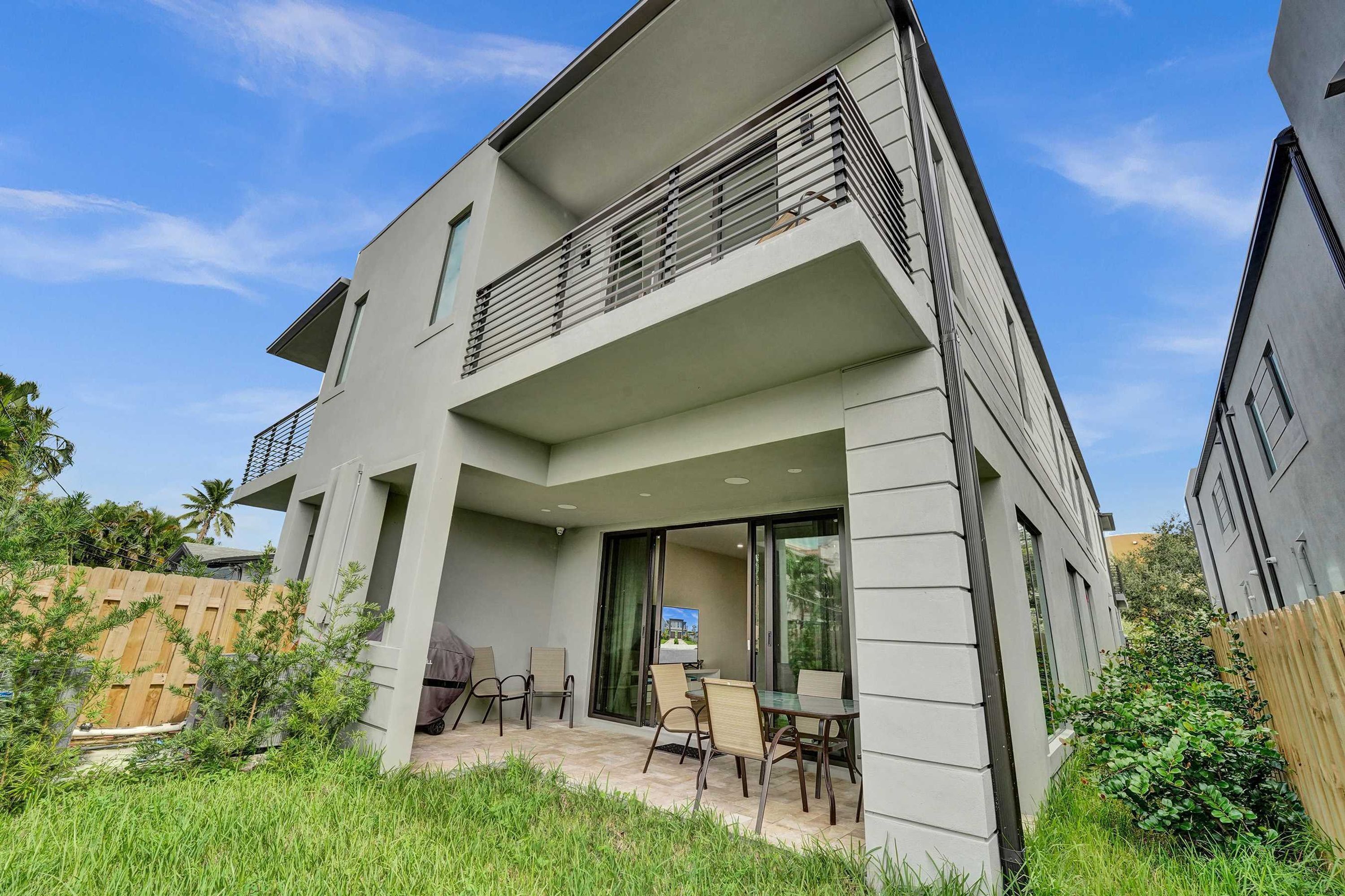 Une maison moderne à deux étages, dotée d’un balcon, d’une terrasse avec mobilier d’extérieur et offrant une vue sur les environs.