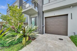 A modern building with a garage door, a balcony, and a well-maintained garden with various plants. - Upscale 4 Bdrm Retreat - Mins to Las Olas Beach (Fort Lauderdale)