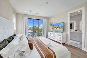 Quarto de hotel moderno com uma cama grande, televisão, varanda e banheiro.