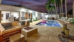 A pool area with lounge chairs, a fire pit, and a swan float. - Waterfront With Pool Spa Tiki Bar and 1 Mile to Beach (Fort Lauderdale)