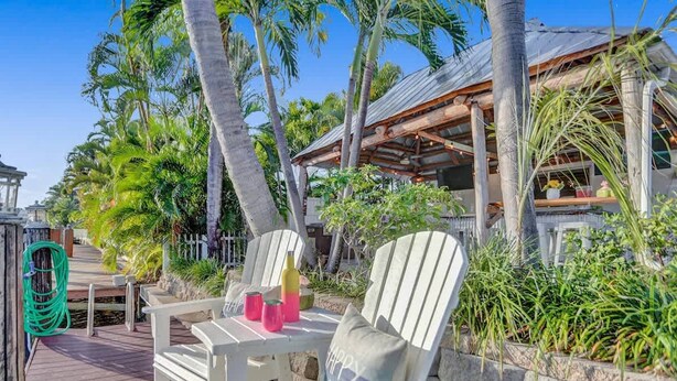 A wooden deck with Adirondack chairs, a small table, and a green garden hose. - Waterfront With Pool Spa Tiki Bar and 1 Mile to Beach (Fort Lauderdale)