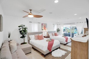 Ein modernes Schlafzimmer mit zwei Betten, einem Deckenventilator und einem großen Fenster.