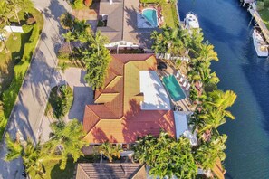 Ein Luftbild eines Anwesens mit Swimmingpool, Bootssteg und einem Gebäude mit rotem Dach, umgeben von Palmen.
