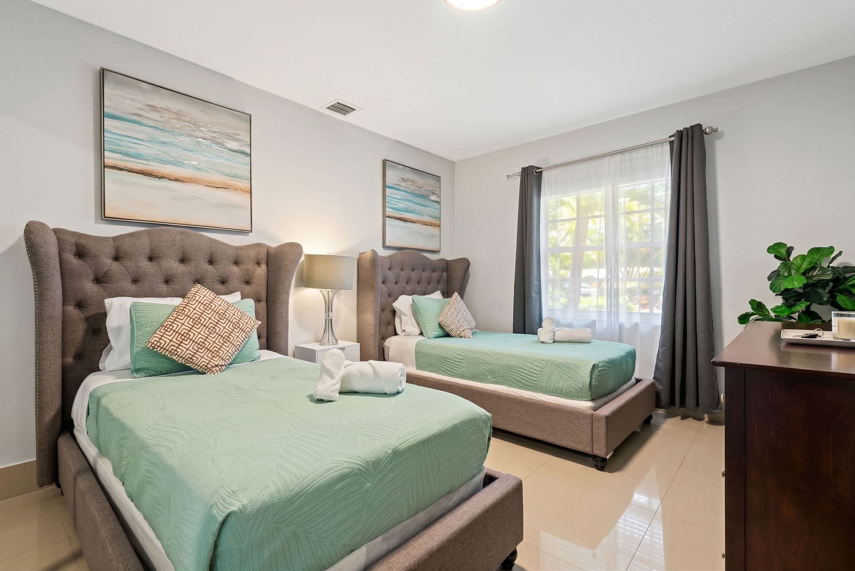 Quarto de hotel com duas camas, uma escrivaninha, uma luminária e obras de arte nas paredes.