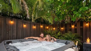 Un bain à remous doté d’une terrasse en bois et illuminé de guirlandes lumineuses, le tout entouré d’une végétation luxuriante.