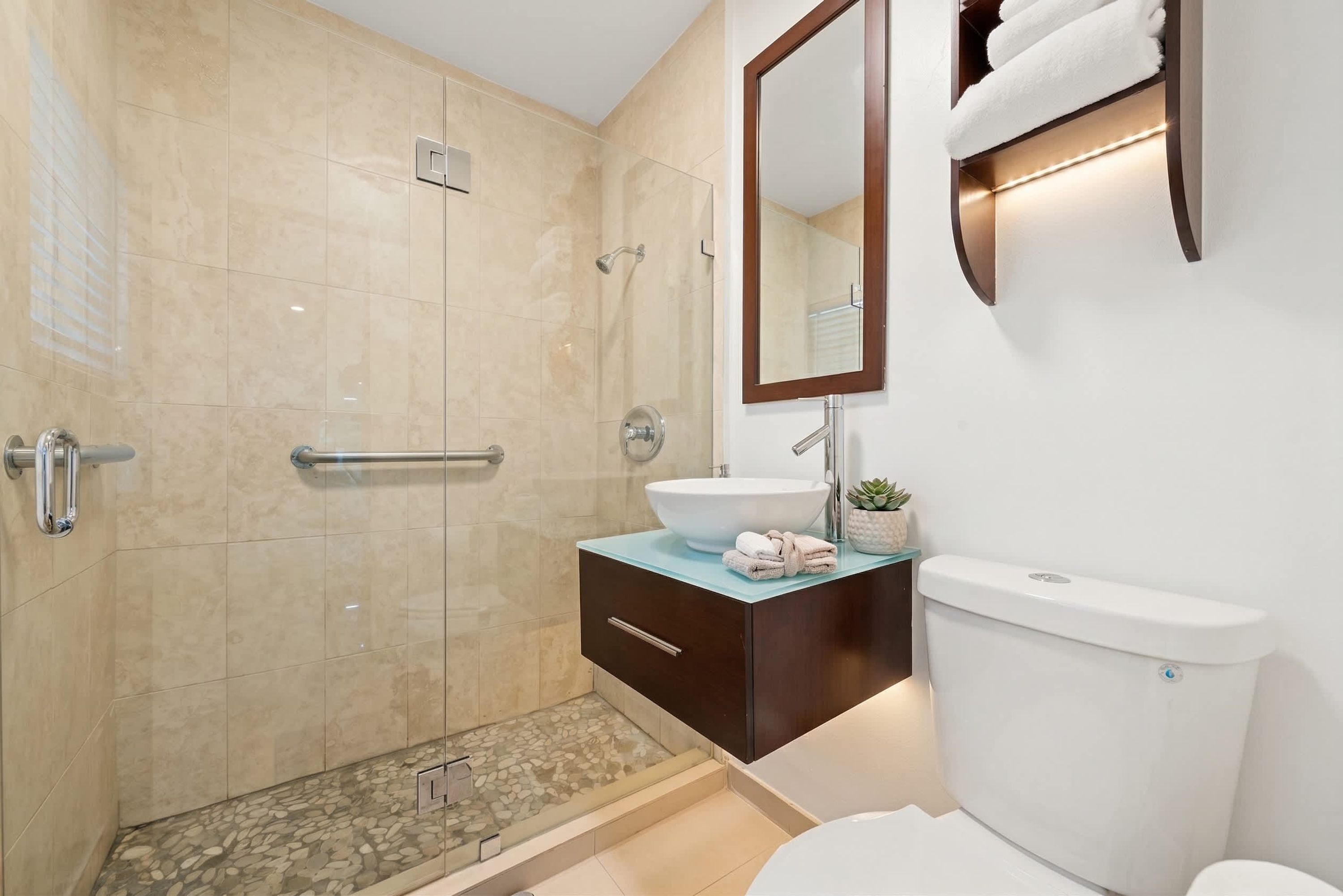A modern bathroom with a glass-enclosed shower, a white sink, and a toilet.