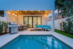 Ein Poolbereich mit Grill, Sitzgelegenheiten und einer überdachten Terrasse.