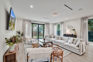 Ein modernes Wohnzimmer mit Sofa, Sesseln, Couchtisch und einem an der Wand befestigten Fernseher.