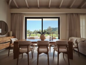 Ein Essbereich mit Tisch, Stühlen, einer Vase und Blick auf eine Landschaft durch ein großes Fenster.