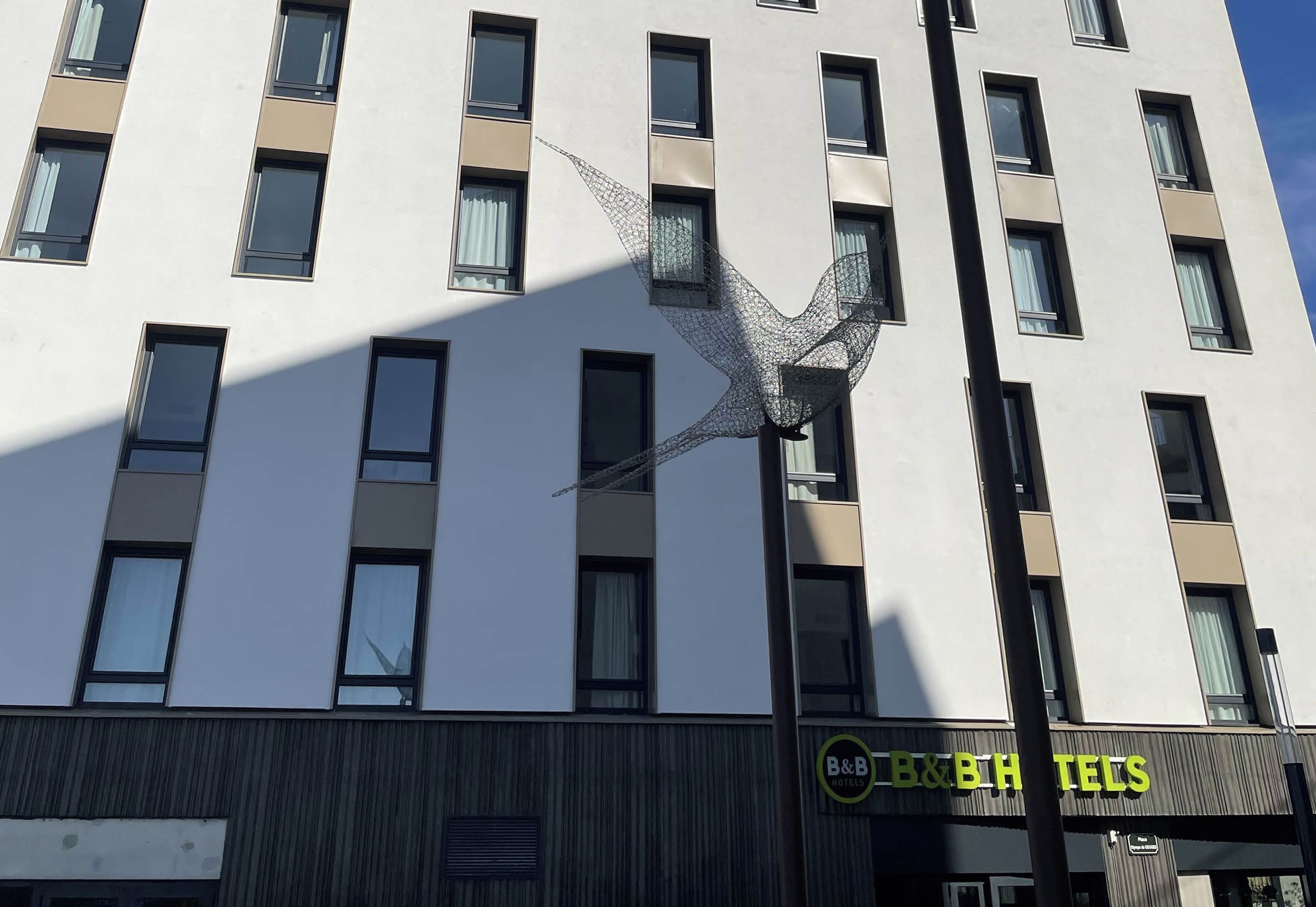 Een hotelgebouw met meerdere ramen en een opvallend draadbeeldhouwwerk aan de gevel.